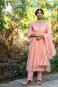 Woman in a peach traditional outfit standing outdoors with greenery in the background
